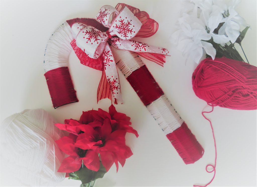 Finished yarn wrapped candy cane wreath laying next to a bouquet of flowers and a ball of yarn | How to Make an Adorable Candy Cane Wreath
