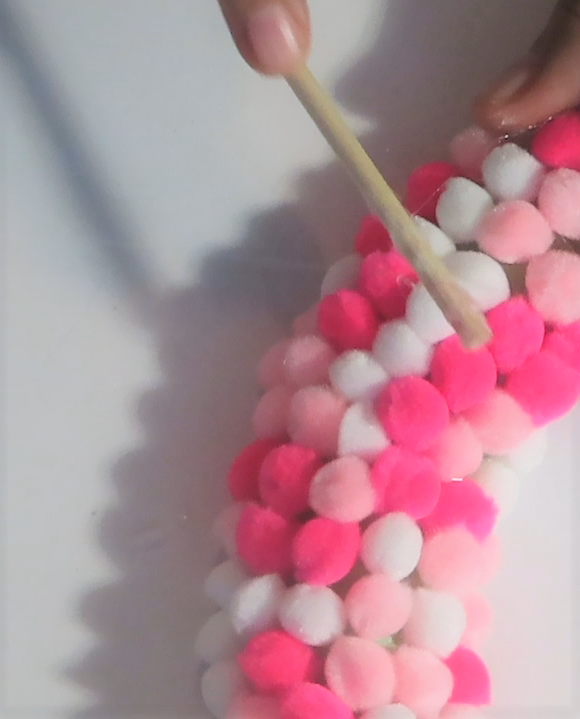 Using a skewer to push the felt pom poms down into the glue | How to Make an Easy Pom Pom Wreath