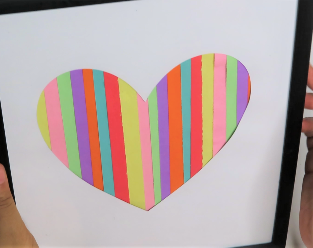 Place the heart cut out on top of the strips of paper and place them in a frame | Colorful DIY Wall Decor for a Stylish Girl's Room