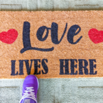 Custom coir Doormat that says "Love Lives Here" with a purple sneaker standing on it
