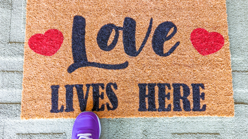 Custom coir Doormat that says "Love Lives Here" with a purple sneaker standing on it