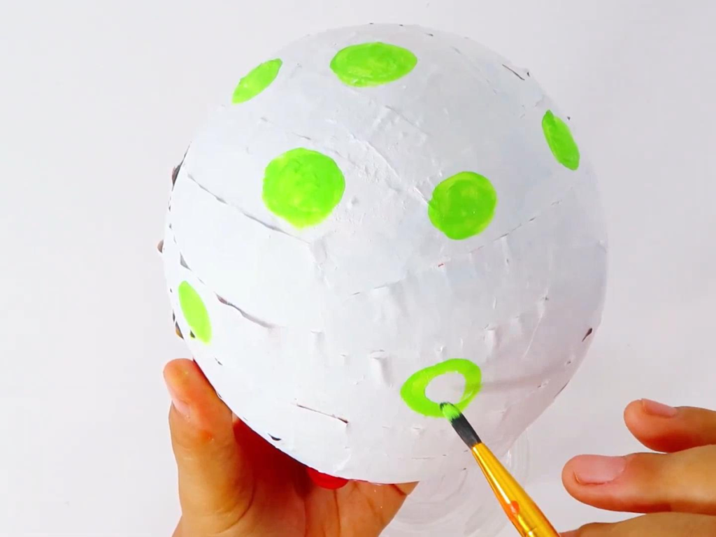 Painting Polka dots on the paper mache dinosaur egg