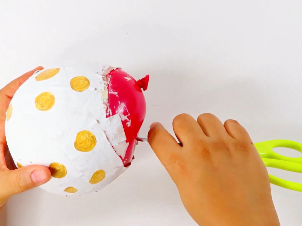 Use your scissors to pop the balloon for the paper mache dinosaur egg