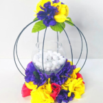 A colorful round floral centerpiece made with a 3d wreath form from Dollar Tree. There are a lot of colorful flowers at the base and a few on top. On the inside is a candle holder with a battery-operated candle and vase filler.
