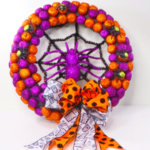 This image shows a DIY Halloween Wreath with glittery Spiders all over it and it has a handmade bow made of two different ribbons.