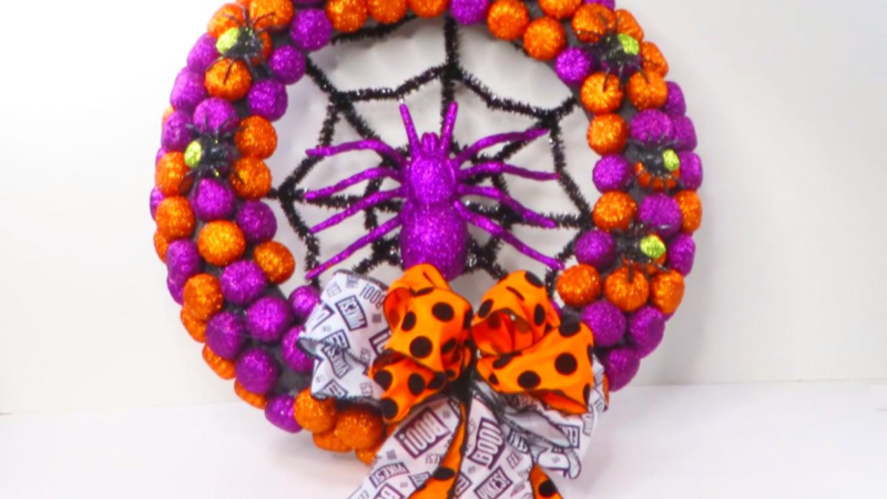 This image shows a DIY Halloween Wreath with glittery Spiders all over it and it has a handmade bow made of two different ribbons.