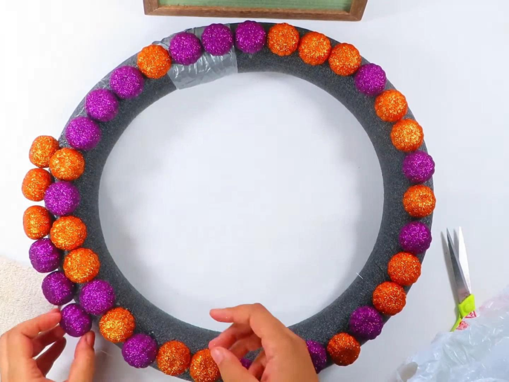 This image shows a pool noodle wreath covered with one and a half rows of purple and orange pumpkin filler