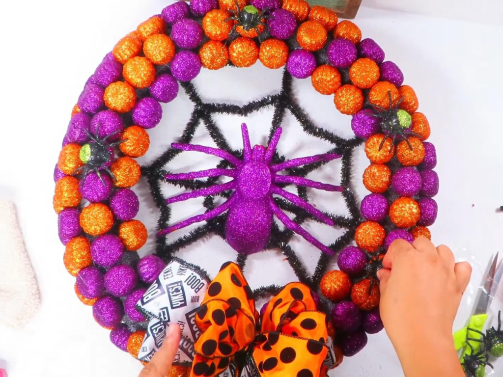 This image shows a hand holding small glitter spiders in place on to the DIY Halloween wreath