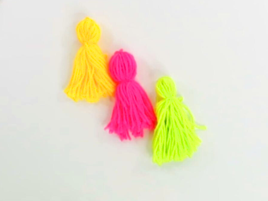 This picture shows three tassels laying beside each other in a diagonal. The left one is yellow, the middle is pink, and the right is lime green.