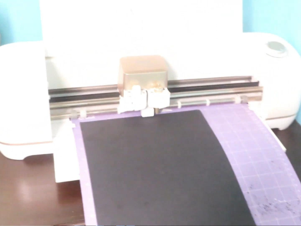 This image shows a Cricut Explore Air 2 cutting a black sheet of cardstock paper