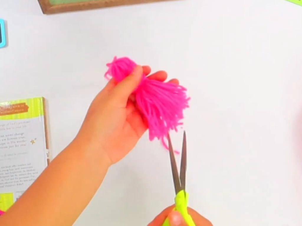 This image shows a hand holding the uneven tassel while the other hand holds of pair of scissors that are cutting the ends of the same tassel to make them even.