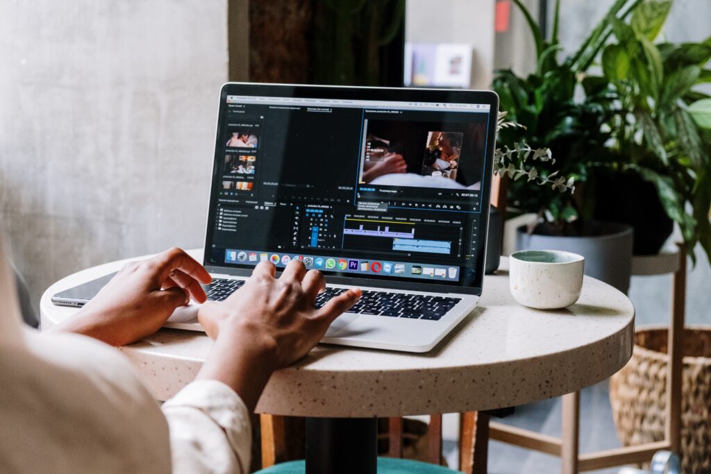 The image shows a person typing on their MacBook Pro on a small white table with plants in the background | The Ultimate Craft App Guide for Crafters of All Ages | Photo by Cottonbro Studio