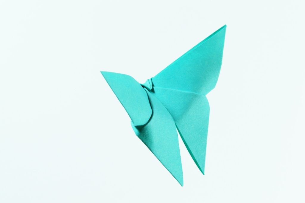 This image shows a turquoise piece of paper that is folded into an origami butterfly. | The Ultimate Craft App Guide for Crafters of All Ages | Photo by Miguel a Padrinan