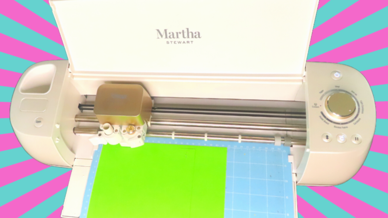 This image shows a Cricut machine with a blue Cricut mat and green paper inside. The back is turquoise and pink striped and comic inspired. | Mind-blowing Cricut crafts to unleash your creativity.