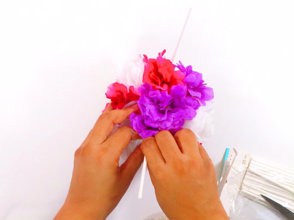 This image shows a pair of hands placing the cake topper sticks into the foam which is inside of the basket / gift box | How to Make a Stunning Hot Air Balloon Centerpiece for Any Occasion