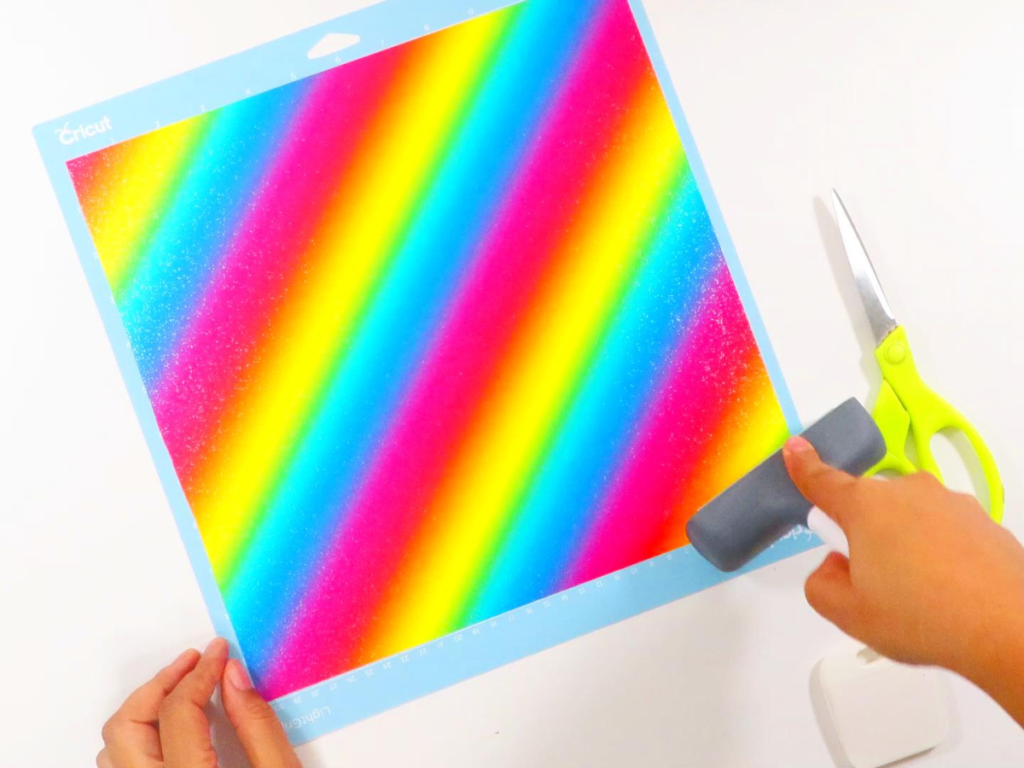 This image shows a 12" square of rainbow sparkle holographic vinyl being smoothed on a Cricut mat with the brayer tool | Personalized Journal Cover Magic with Cricut