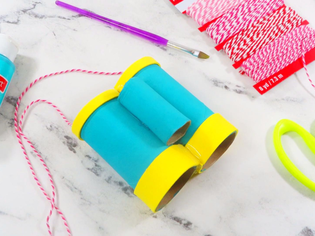 This image shows turquoise toilet paper roll binoculars with yellow accents laying on a white marble surface | How to Make Toilet Paper Roll Binoculars in a Few Easy Steps