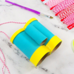 This image shows turquoise toilet paper roll binoculars with yellow accents laying on a white marble surface | How to Make Toilet Paper Roll Binoculars in a Few Easy Steps