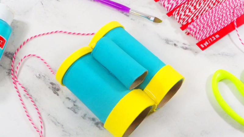 This image shows turquoise toilet paper roll binoculars with yellow accents laying on a white marble surface | How to Make Toilet Paper Roll Binoculars in a Few Easy Steps