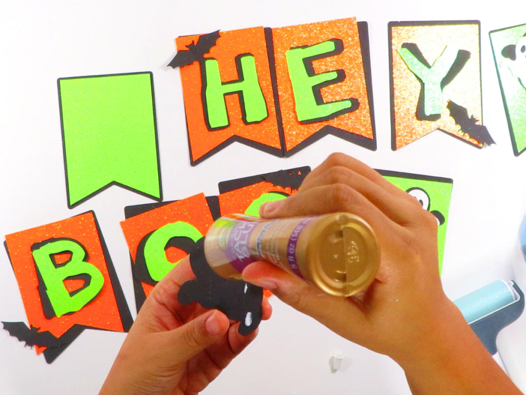 This image shows someone gluing the paper bats to the "Hey Boo" Halloween Banner | How to Make a Banner for Halloween That's Cute and Spooky