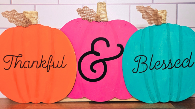 3 wooden pumpkins painted orange, pink, and turquoise with the words Thankful & Blessed written on them with black permanent vinyl