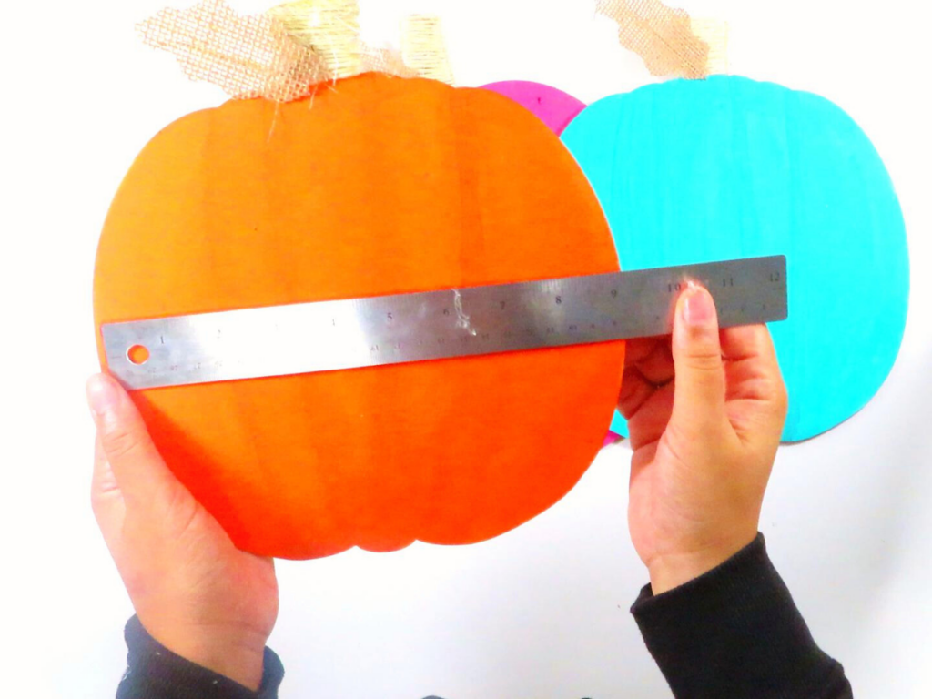 Measuring the width of the painted wooden pumpkins