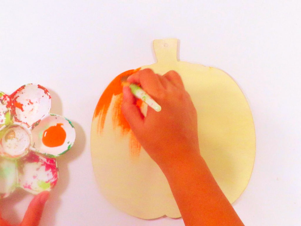 This image shows painting the wooden pumpkins with Orange Spice by Craftsmart | DIY Fall Decor You'll Love Making with Simple Decor